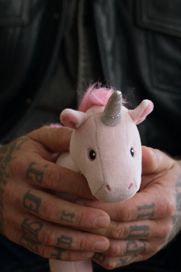 The Biker’s Right Hand Had “Death” Tattooed Across The Knuckles, But Inside The Courthouse Hallway He Was Holding A Tiny Pink Stuffed Unicorn Like It Was The Most Breakable Thing God Had Ever Trusted Him With.